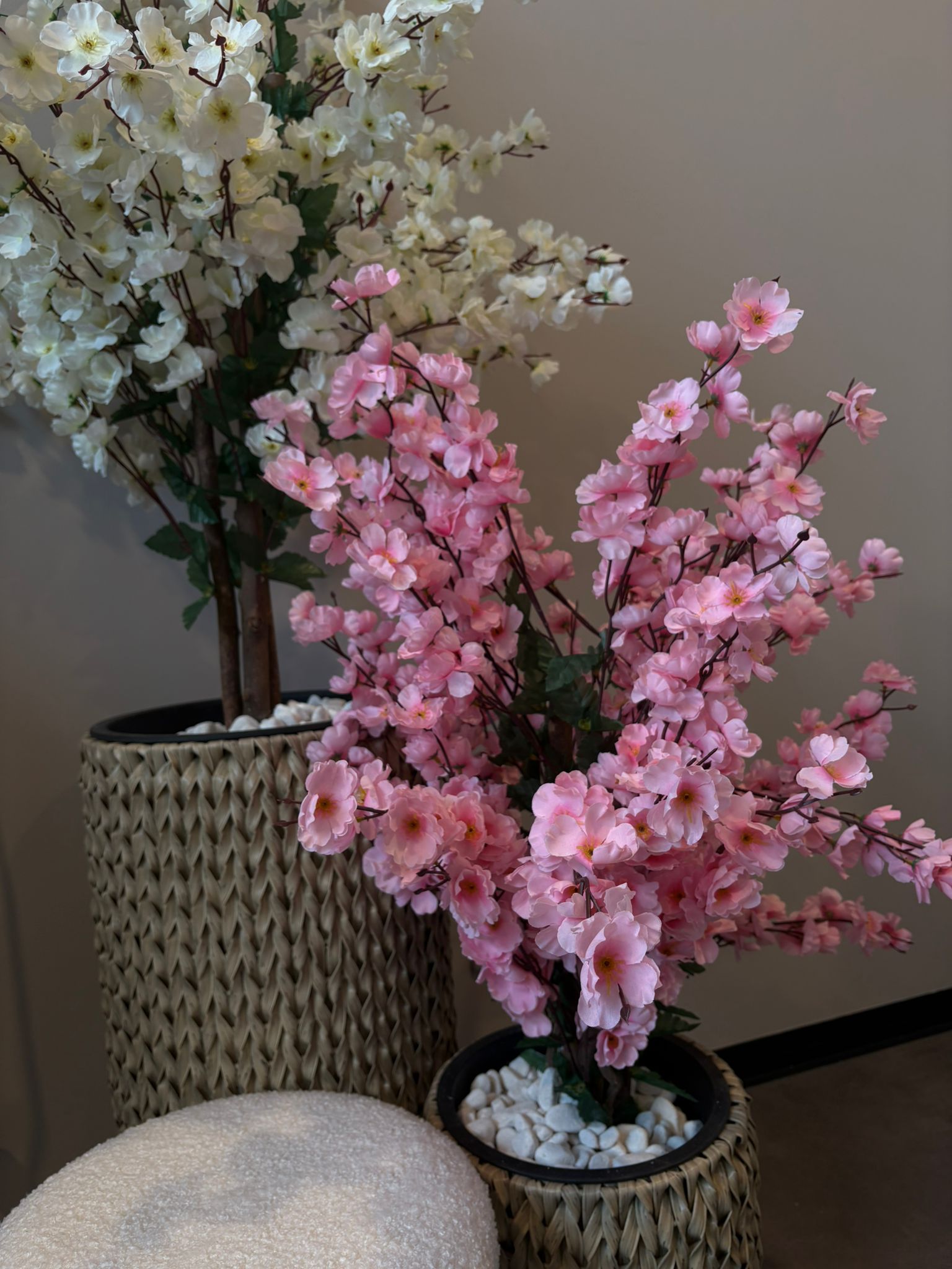 Roze en witte bloesemtakken in gevlochten plantenbakken naast een bouclé kruk